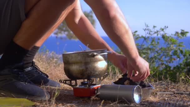 Seorang pria berkemah, memasak makanan di samping tenda di tepi garis pantai yang curam di hutan pinus dengan pemandangan indah lanskap laut. 4k — Stok Video
