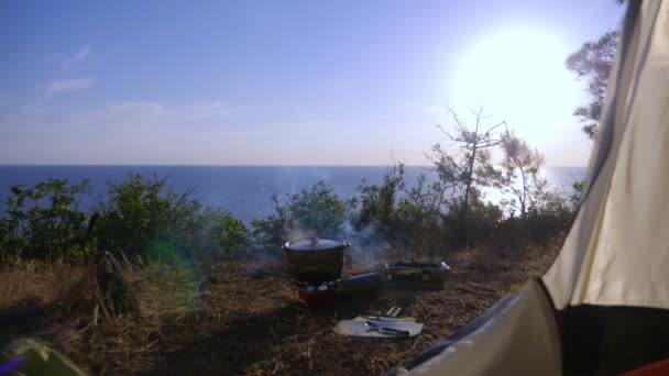 一个投球手和一次性烧烤架。在松树林的陡峭海岸线边缘的一个帐篷边做饭, 看到了壮观的海景色。4k. — 图库视频影像