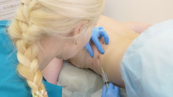 Le médecin le dermatologue le cosmétique introduit la lipolitique au moyen d'une seringue dans les plis gras sur le dos de la femme du patient. 4k — Video