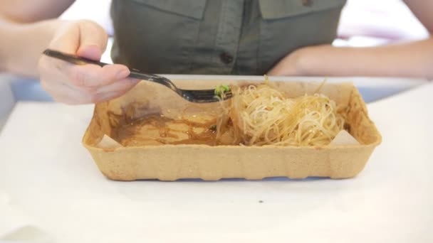 Gebratene Nudeln mit Brokkoli, Bohnen und Huhn umrühren. Eine Frau isst in einem Lebensmittelladen Lebensmittel aus Einweggeschirr. 4k — Stockvideo