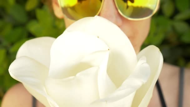 Uma bela flor de magnólia branca nas mãos de uma mulher no rosto. reflexão em óculos de sol, close-up. 4k, câmera lenta — Vídeo de Stock