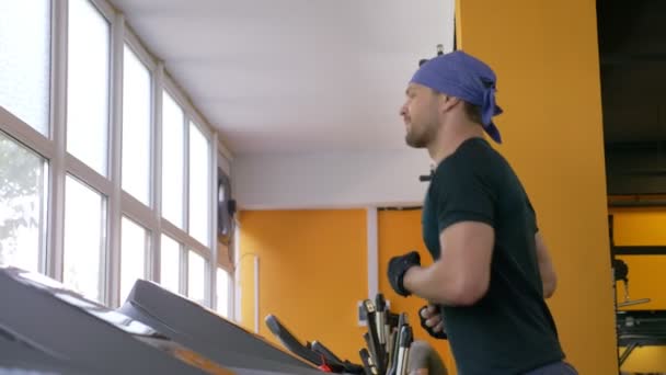 Een leuke vent draait op een loopband in de sportschool. 4k, slow-motion — Stockvideo