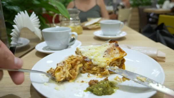 Un hombre come lasaña en un restaurante con tenedor y cuchillo. Primer plano. 4k, cámara lenta — Vídeo de stock