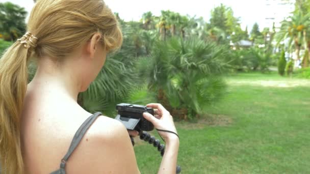 Profesionální fotograf, fotografie krása tropického parku, Žena stiskne tlačítko miniaplikace uprostřed kvetoucí zahrady. 4k, pomalý pohyb — Stock video