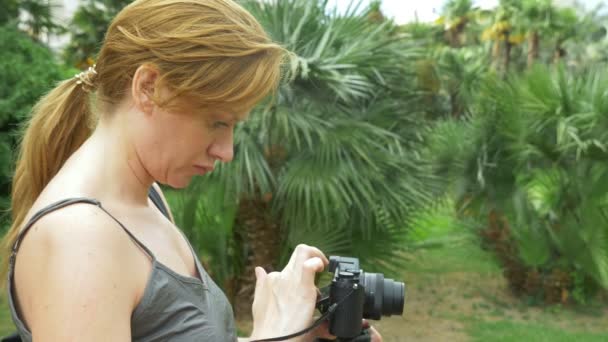 一个专业摄影师, 照片的美丽的热带公园, 一个女人按一个小工具的按钮, 在一个开花的花园。4k. 慢动作 — 图库视频影像
