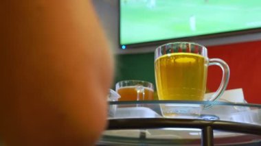 Yerel barda televizyonda futbol maçı izliyor. Gıda, bira. bir kupa bira odak ile bir Tv ekranında bir yayın bir futbol ile bulanıklık. 4k