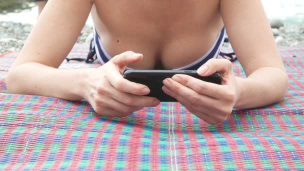 Menina na praia usando um smartphone. mulher sexy em um biquíni. 4k — Vídeo de Stock