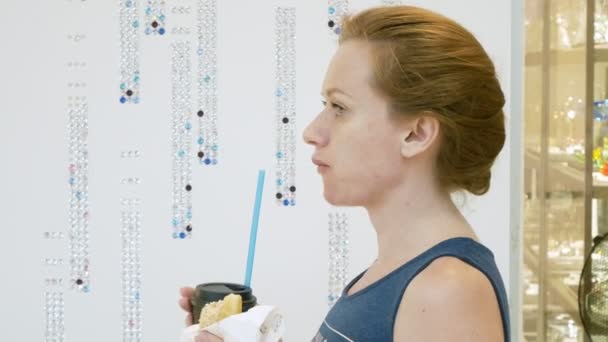 Женщина ест пончик и пьет кофе через соломинку в торговом центре. 4k — стоковое видео