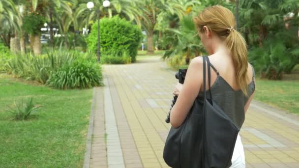 Fotografo professionista, fotografa la bellezza di un parco tropicale, una donna preme un pulsante di un gadget tra un giardino fiorito. 4k, rallentatore — Video Stock