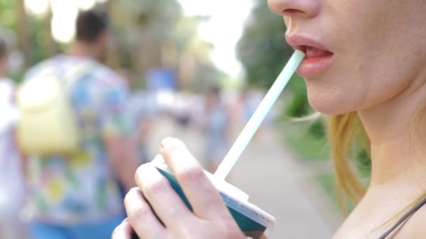 Женские губы сексуально пьют коктейль из трубки на фоне людей, отдыхающих и гуляющих в городском парке. 4k, slow motion — стоковое видео