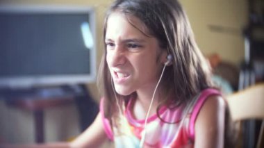 küçük kız esmer kulaklıklar, uzun saçlı bilgisayar başında oturan şarkı söylüyor. 4k, ağır çekim