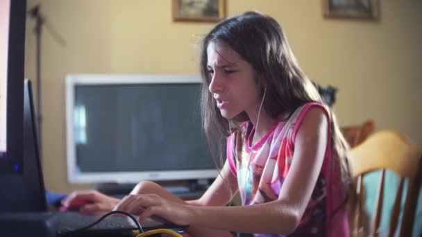 Kis lány barna, hosszú haj, a fejhallgató, énekel dalokat számítógép előtt ül. 4k, lassú mozgás — Stock videók