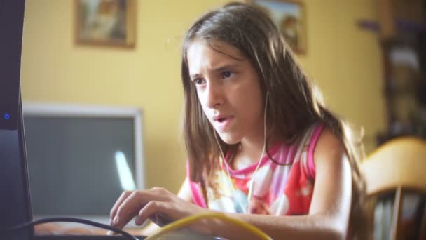 Kleine meisje brunette met lange haren op koptelefoon, zingt liedjes zitten voor de computer. 4k, slow-motion — Stockvideo