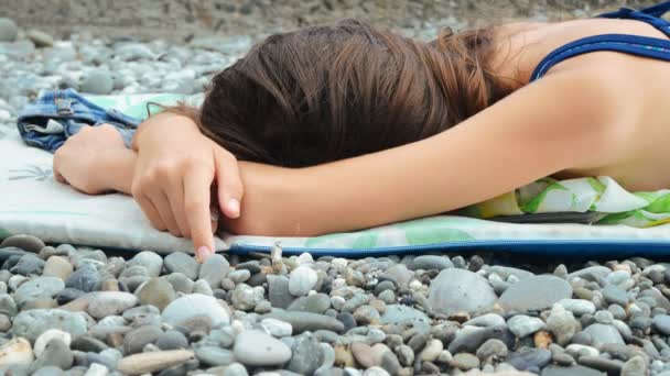 Una ragazza stanca giace su una riva rocciosa, si copre il viso con le mani. 4k — Video Stock