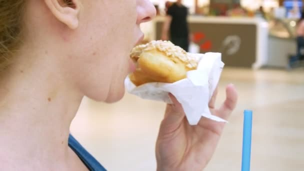 A mulher está a comer um donut e a beber café com palhinhas no centro comercial. 4k — Vídeo de Stock