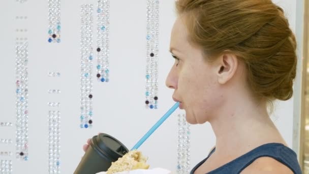 Kvinden spiser en donut og drikker kaffe gennem sugerør i indkøbscentret. 4k – Stock-video