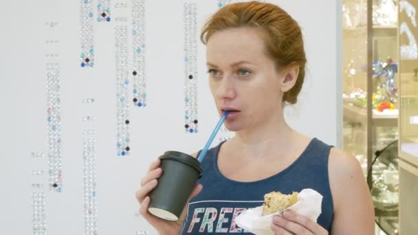 La mujer está comiendo un donut y bebiendo café a través de pajitas en el centro comercial. 4k — Vídeo de stock