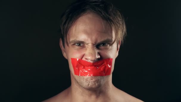 Young man with taped mouth. on a black background. 4k. — Stock Video