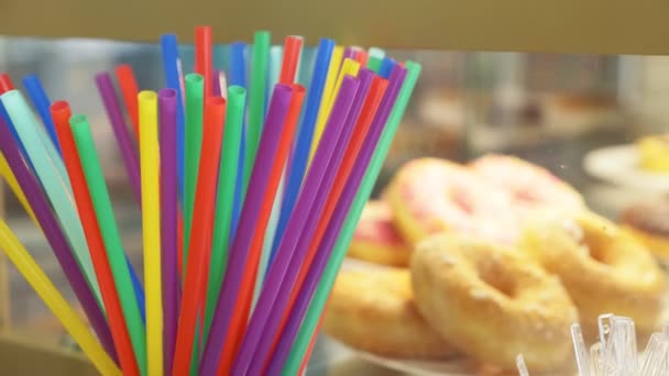 Palhas coloridas de bebidas no contexto de rosquinhas em uma janela de loja de uma confeitaria. 4k, câmera lenta — Vídeo de Stock