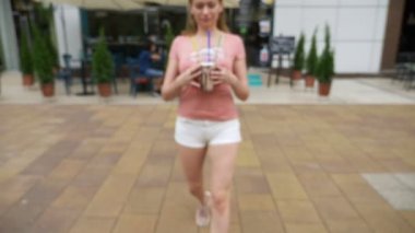 Gözlük smoothies ve kokteyller ile tutarak yaya cadde boyunca kız yürüyor. bulanıklık, 4 k, yakın çekim, ağır çekim
