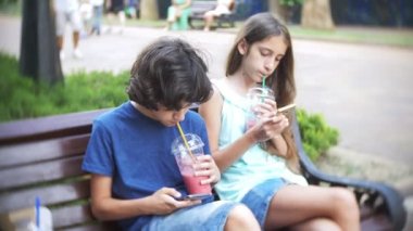 kavram internet bağımlılığı, genç erkek ve kız parkta bir bankta sadece yürüyüş ve hayattan zevk yerine bir yaz gününde kambur oturma onların akıllı telefonlar kullanmak. 4k, ağır çekim