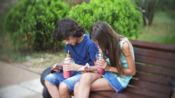 Έννοια του εθισμού στο διαδίκτυο, Έφηβος αγόρι και κορίτσι χρησιμοποιήσει τα smartphone τους, κάθεται καμπούρα σε ένα παγκάκι στο πάρκο σε μια καλοκαιρινή μέρα, αντί απλά περπατώντας και απολαμβάνοντας τη ζωή. 4k, αργή κίνηση — Αρχείο Βίντεο