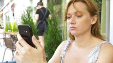 izlerken memnun kız sokakta bir kafede oturup telefon