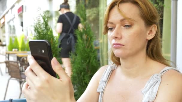 不満を持って女の子を見る通りのカフェに座っている携帯電話 — ストック動画