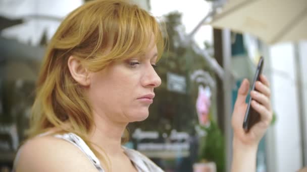 Missnöjd tjej tittar på telefon sitter på ett café på gatan — Stockvideo
