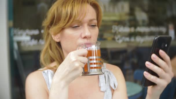 The girl is drinking tea with Sitting in a summer cafe. Transparent glass. — Stock Video