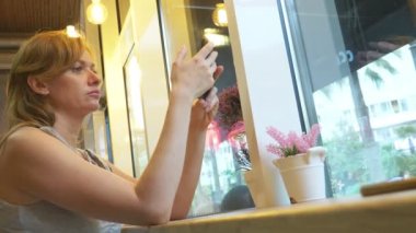 seyir telefon tatminsiz kız tek başına büyük bir panoramik pencere, 4 k yakın bir kafede oturmak