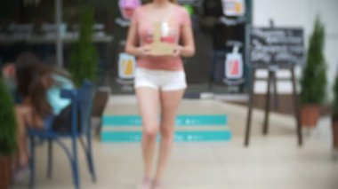 Gözlük smoothies ve kokteyller ile tutarak yaya cadde boyunca kız yürüyor. bulanıklık, 4 k, yakın çekim, ağır çekim