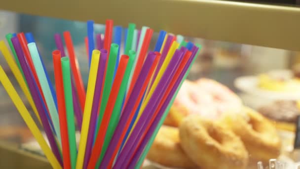 Las pajitas coloridas para las bebidas sobre el fondo de las rosquillas en el escaparate de la confitería. 4k, cámara lenta — Vídeos de Stock