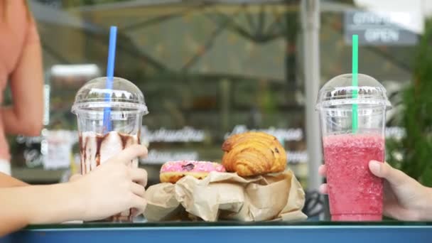 Desayuno útil. primer plano, las manos tintinean vasos con fresco en el fondo de un café de la calle. pasteles frescos en la mesa. 4k, cámara lenta . — Vídeos de Stock