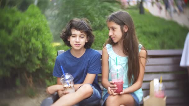 Chlapec a dívka dospívající sedí na lavičce, v ruce drží brýle s fresh a smoothie. 4 k. Zpomalený pohyb. — Stock video