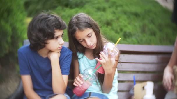 Fiú és lány tinédzser ül egy padon, üvegek, turmixok és friss a kezében tartja. 4 k. lassú mozgás. — Stock videók