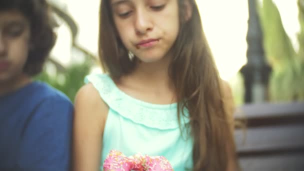 Sad boy and teen girl sitting on bench holding glasses with fresh and smoothies in hand. eat a donut and a croissant of 4k. Slow motion. — Stock Video