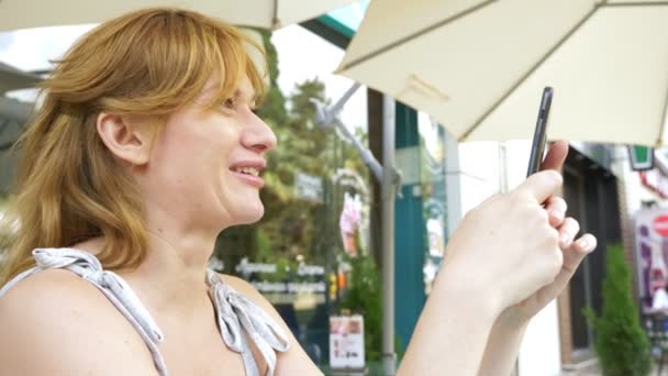 Kobieta, trzymając smartfon na ulicy. siedząc w kawiarni lato — Wideo stockowe