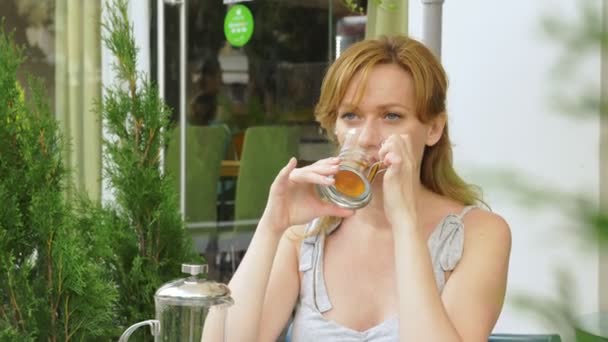 Het meisje is het drinken van thee met zithoek in een zomerterras. Transparant glas. — Stockvideo