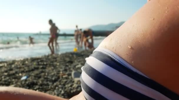 Jovem bela menina bronzeada sexy em biquíni deitado na praia junto ao mar. Vista do mar através do peito feminino. 4k — Vídeo de Stock