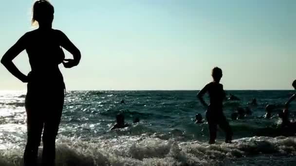 Silhouette dell'irriconoscibilità delle persone che riposano sulla spiaggia durante il tramonto . — Video Stock