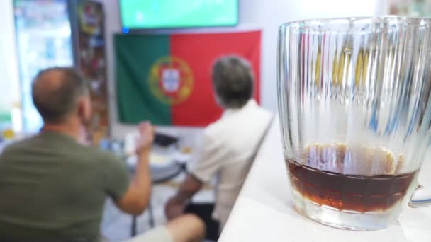 A ver futebol na televisão no pub local. Comida, cerveja. uma caneca com cerveja em foco, uma tela de TV com uma transmissão de um borrão de futebol. 4k — Vídeo de Stock