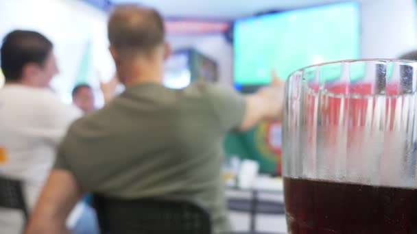 Watching football game on television at local pub. Food, beer. a mug with beer in focus, a TV screen with a broadcast of a football blur. 4k — Stock Video