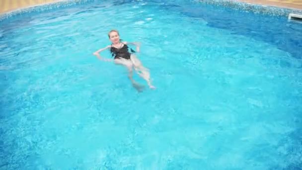 黒の水着でセクシーな女性はプールで泳ぎます。スローモーション。4 k. — ストック動画