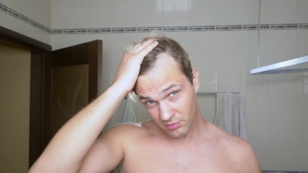 Joven hombre atractivo inspecciona una línea de cabello en retroceso en el baño. Calvicie — Vídeos de Stock
