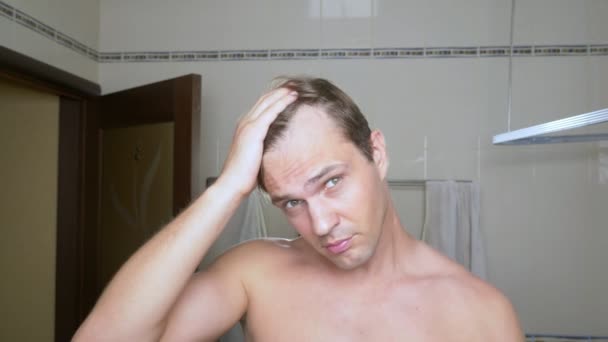 Giovane uomo attraente ispeziona un reclinazione dei capelli in bagno. Calvizie — Video Stock