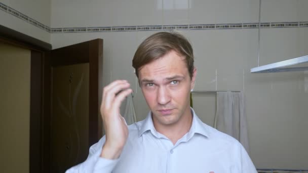 Mladý atraktivní muž kontroluje ustupující vlasovou linkou, v koupelně. Plešatost — Stock video