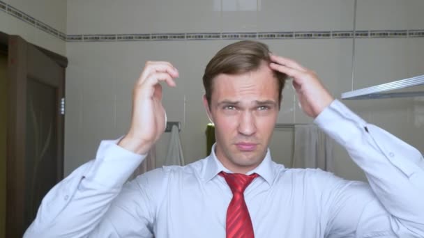 Joven hombre atractivo inspecciona una línea de cabello en retroceso en el baño. Calvicie — Vídeo de stock