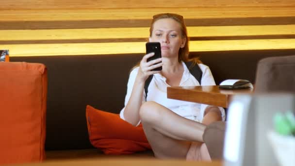 Una turista utiliza un teléfono mientras espera un pedido en un café. 4k — Vídeos de Stock