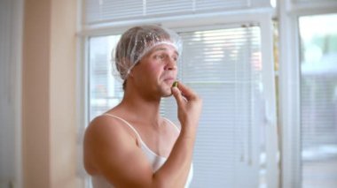 Yüz paketi olan garip adam. Genç bir adam bir ev bir ayna önünde yüz için kozmetik işlemler yapar. 4k